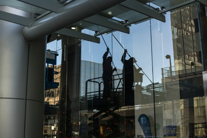 onderhoudsman die op een schaarlift staat en een glazen raam schoonmaakt